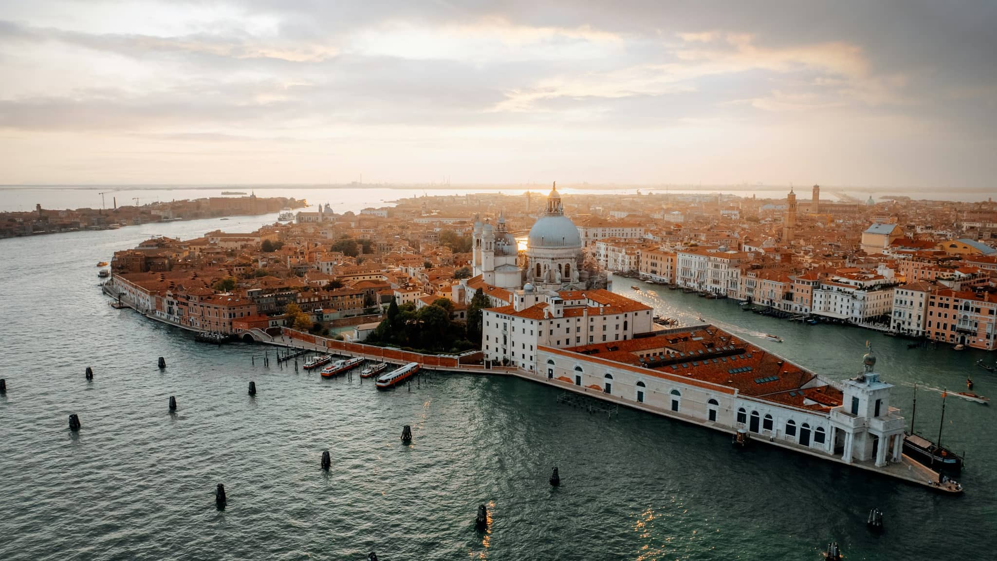 Visitors crossing a Venice bridge on a busy spring afternoon, the lagoon light low on the water.