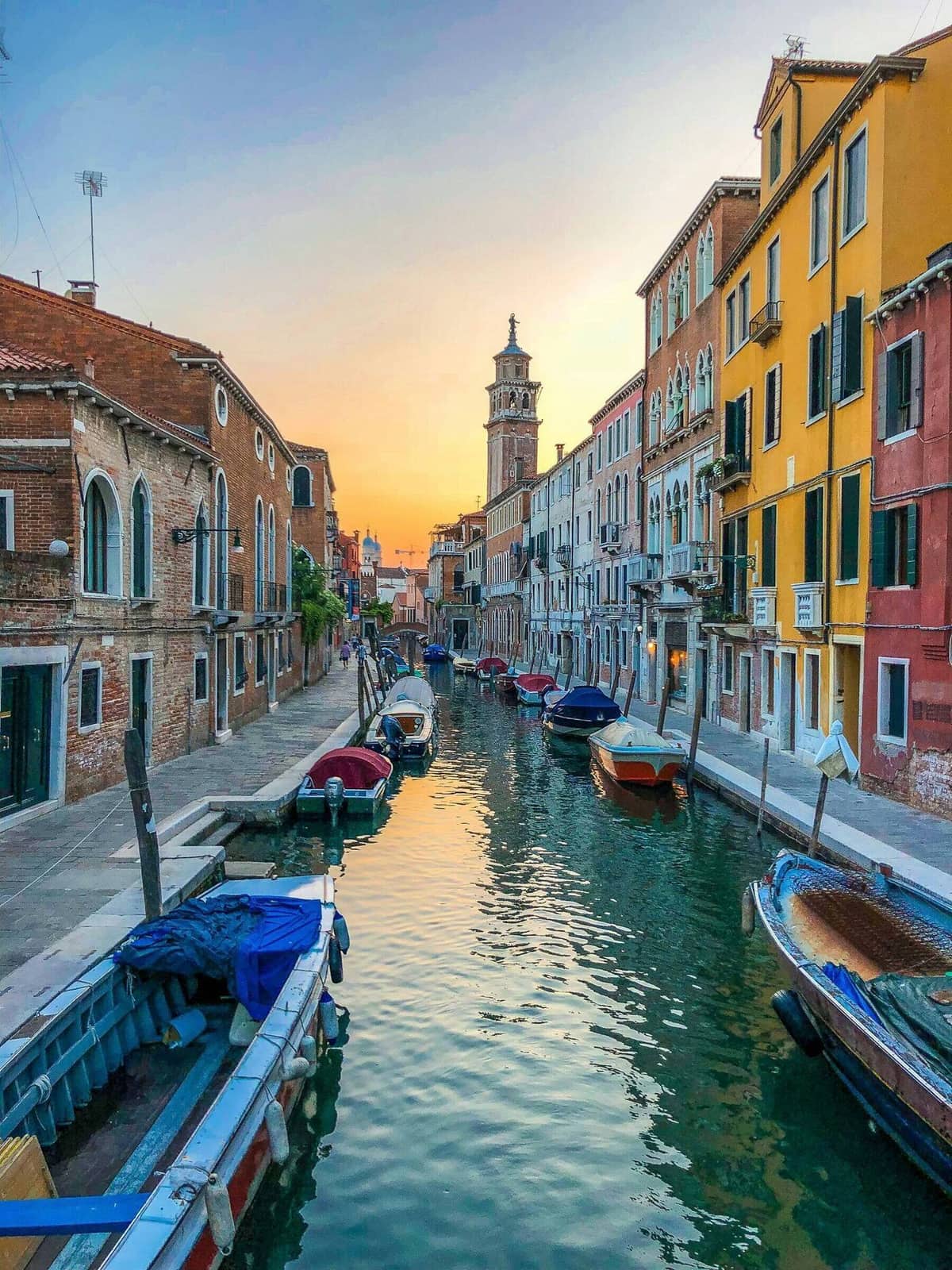 A working boat moves along a Cannaregio canal in low afternoon light, residential facades on the opposite bank.